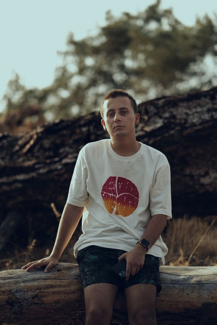 Casual portrait of a young man sitting on a log, enjoying leisure time outdoors.