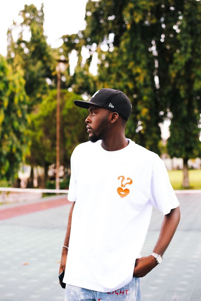 Young man with cap in casual summer outfit stands outdoors, exuding urban style.