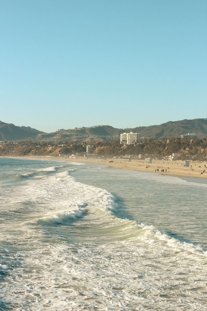 Beautiful sunny day at Santa Monica Beach with gentle waves and distant mountains in California.