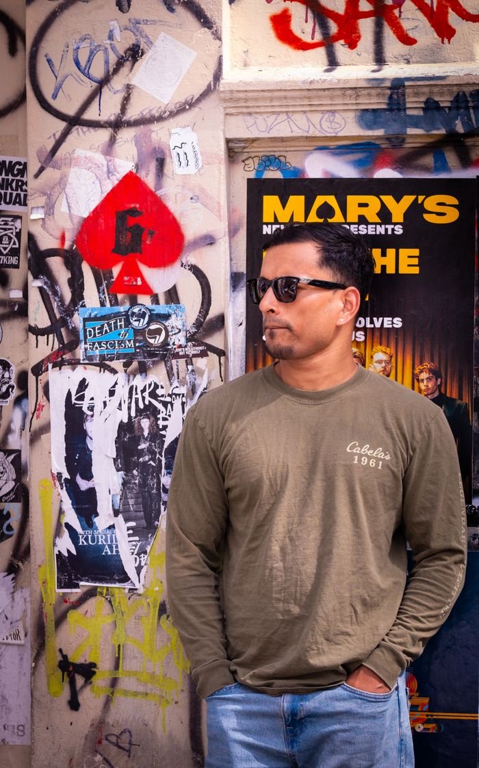 Casual man in sunglasses posing by a graffiti-covered wall with posters.