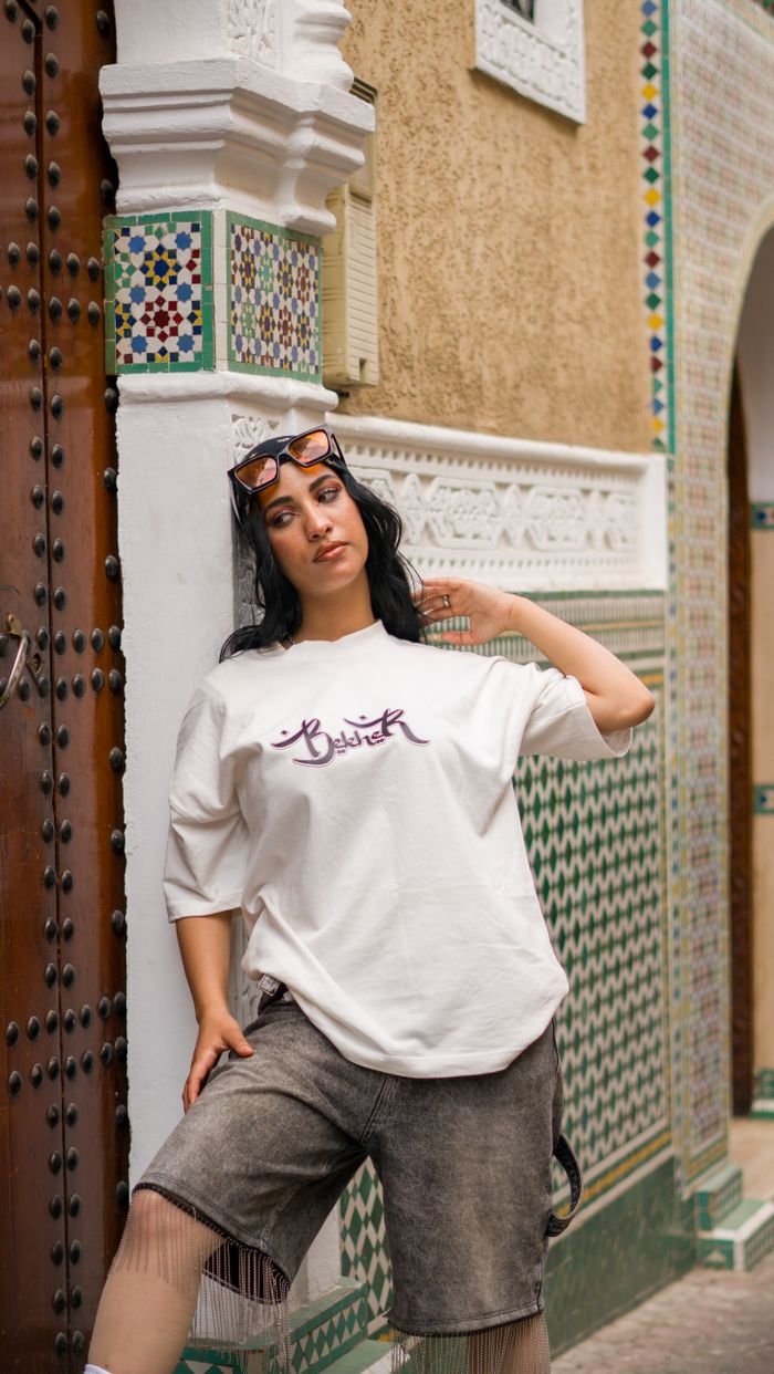 A woman poses casually in front of intricate Moroccan architecture wearing modern casual fashion.